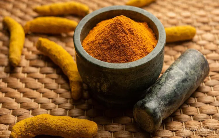 زردچوبه سابیده‌شده درون هاون سیاه در کنار زردچوبه قلم